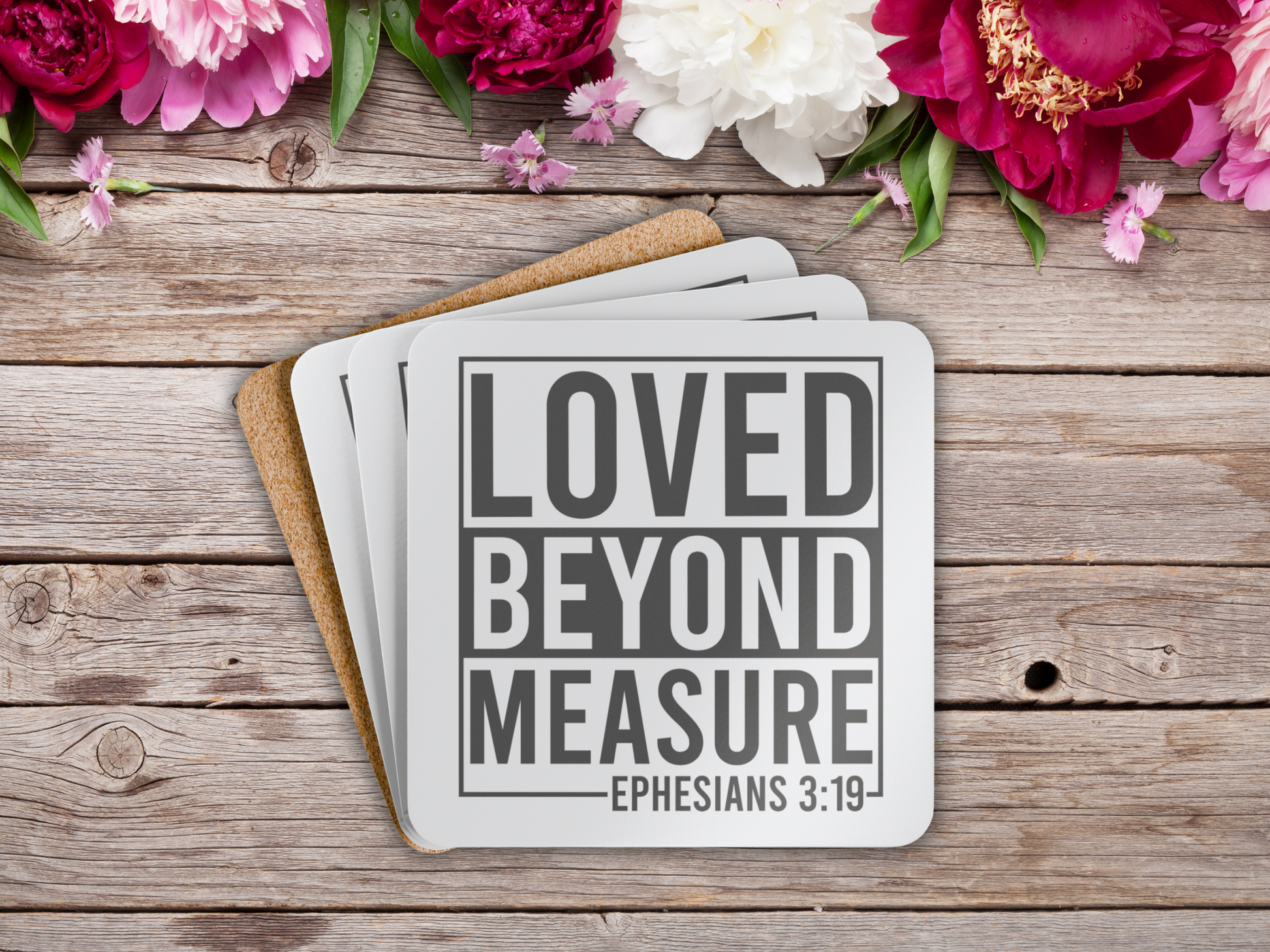 Scripture coasters stacked on rustic wooden surface, styled with vibrant pink and white flowers.