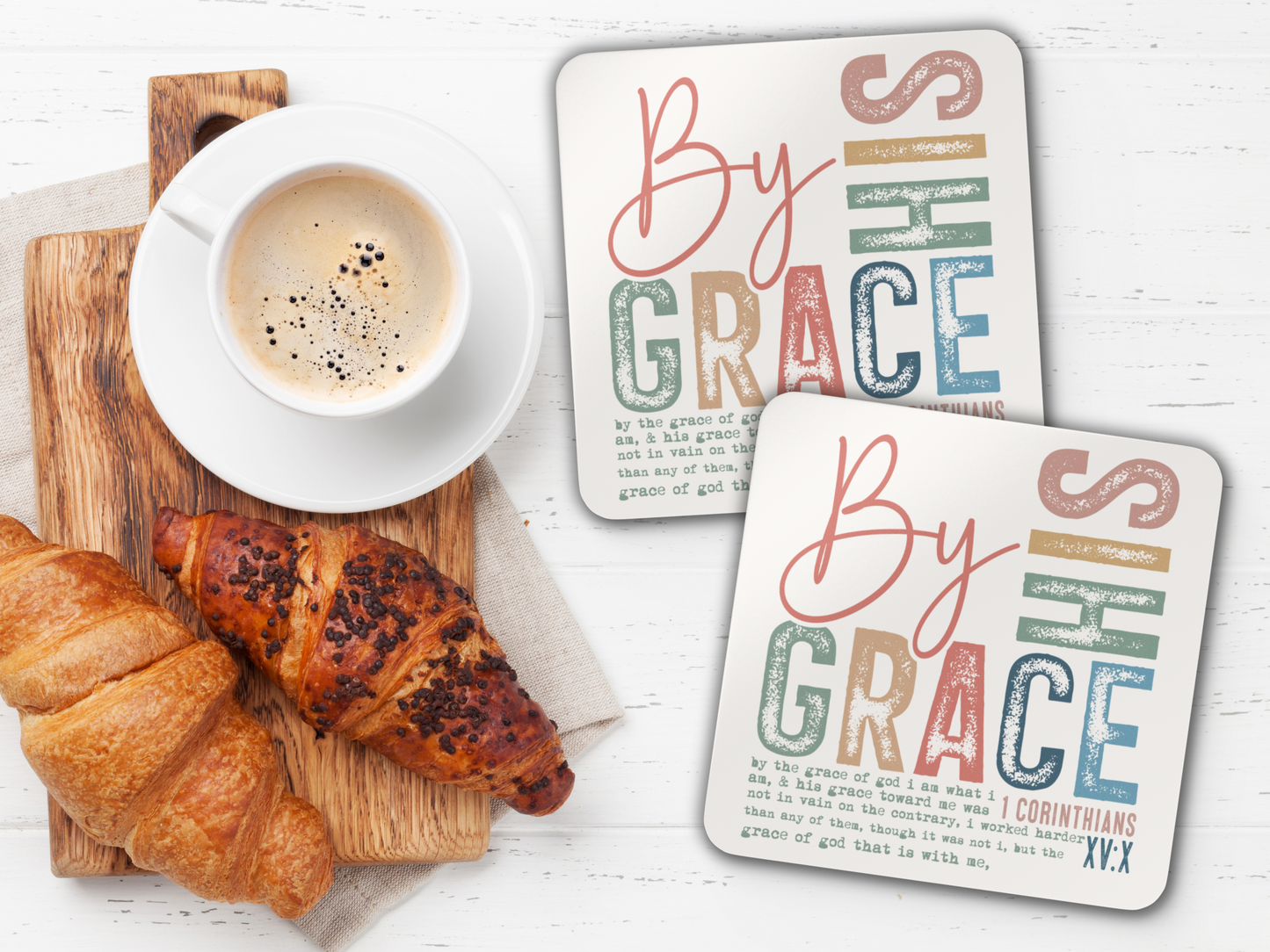 Pair of scripture coasters with coffee and croissants on wooden serving board over white table.