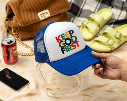 Blue and white cap with 'Keep God First' text held by a hand, with a phone, soda can, and sandals in the background.