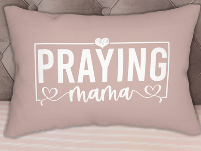 Christian decorative lumbar pillow reading “Praying Mama,” placed against tufted headboard on striped bedding.