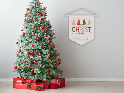 Decorated Christmas tree with red ornaments and presents, next to a 'Merry Christmas' wall banner on a plain wall.