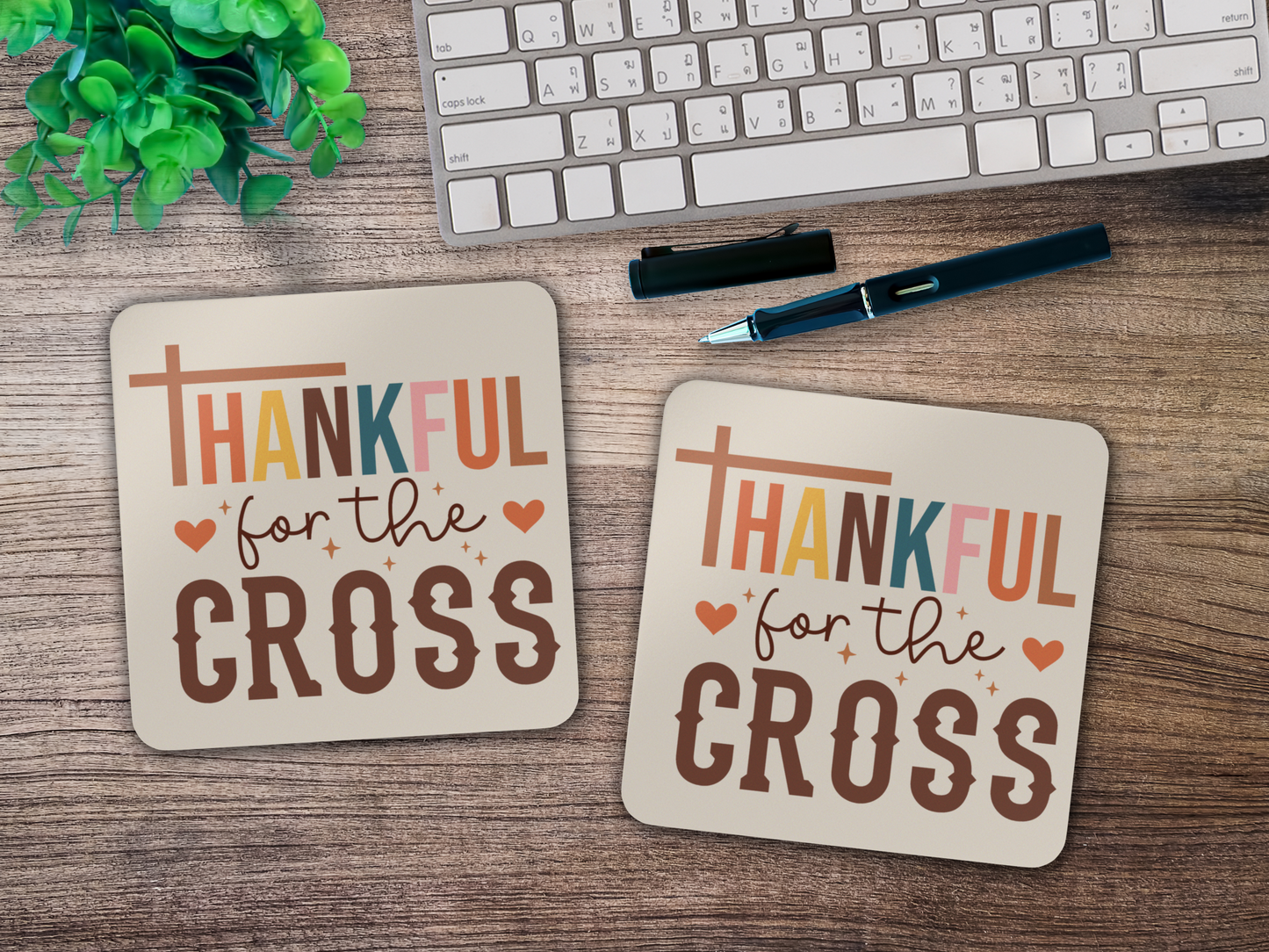 Two “Thankful for the Cross” coasters styled on a wooden desk with keyboard, pen, and green plant.