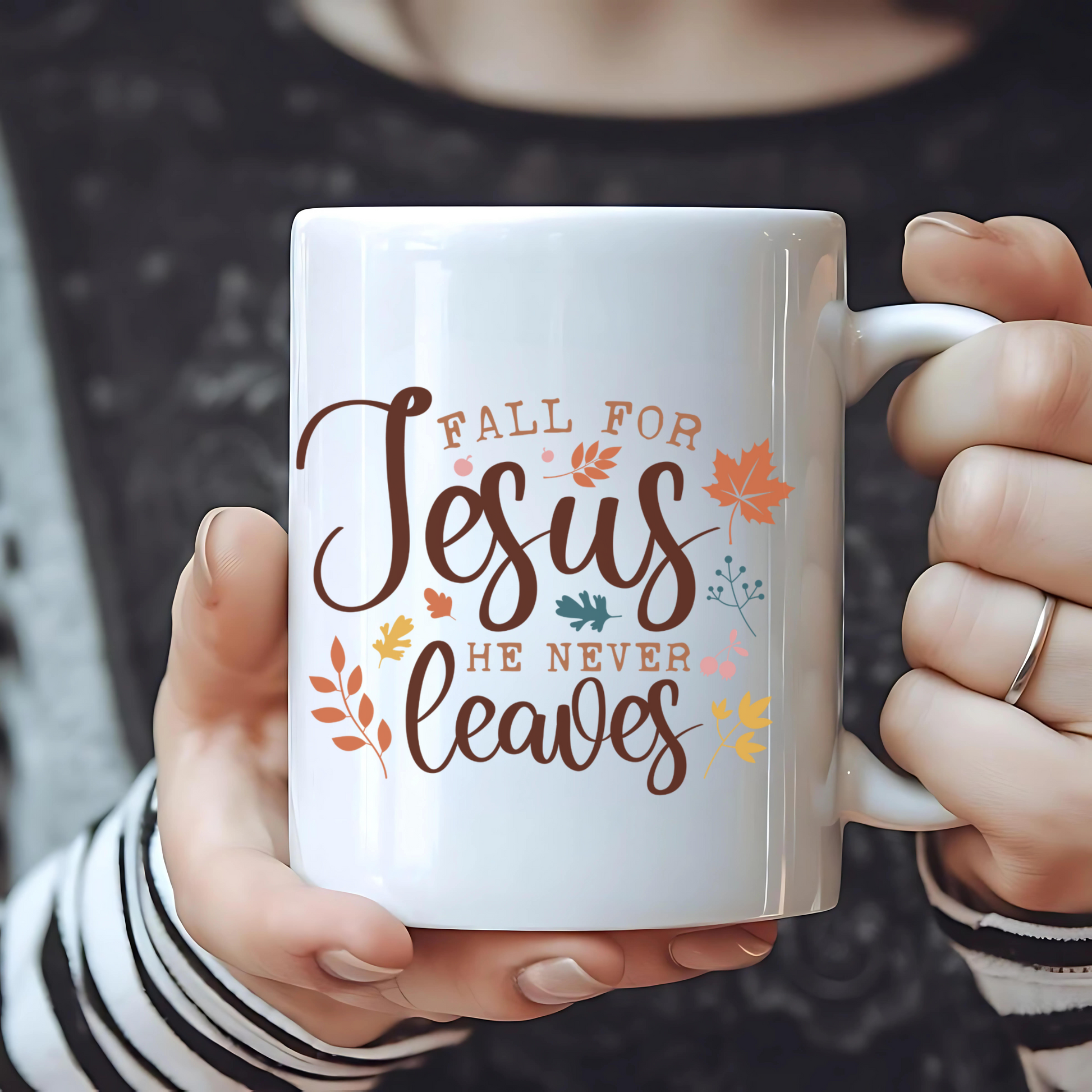 Person holding a white mug with 'Fall for Jesus he never leaves' text and autumn leaves design.