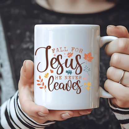 Person holding a white mug with 'Fall for Jesus he never leaves' text and autumn leaves design.