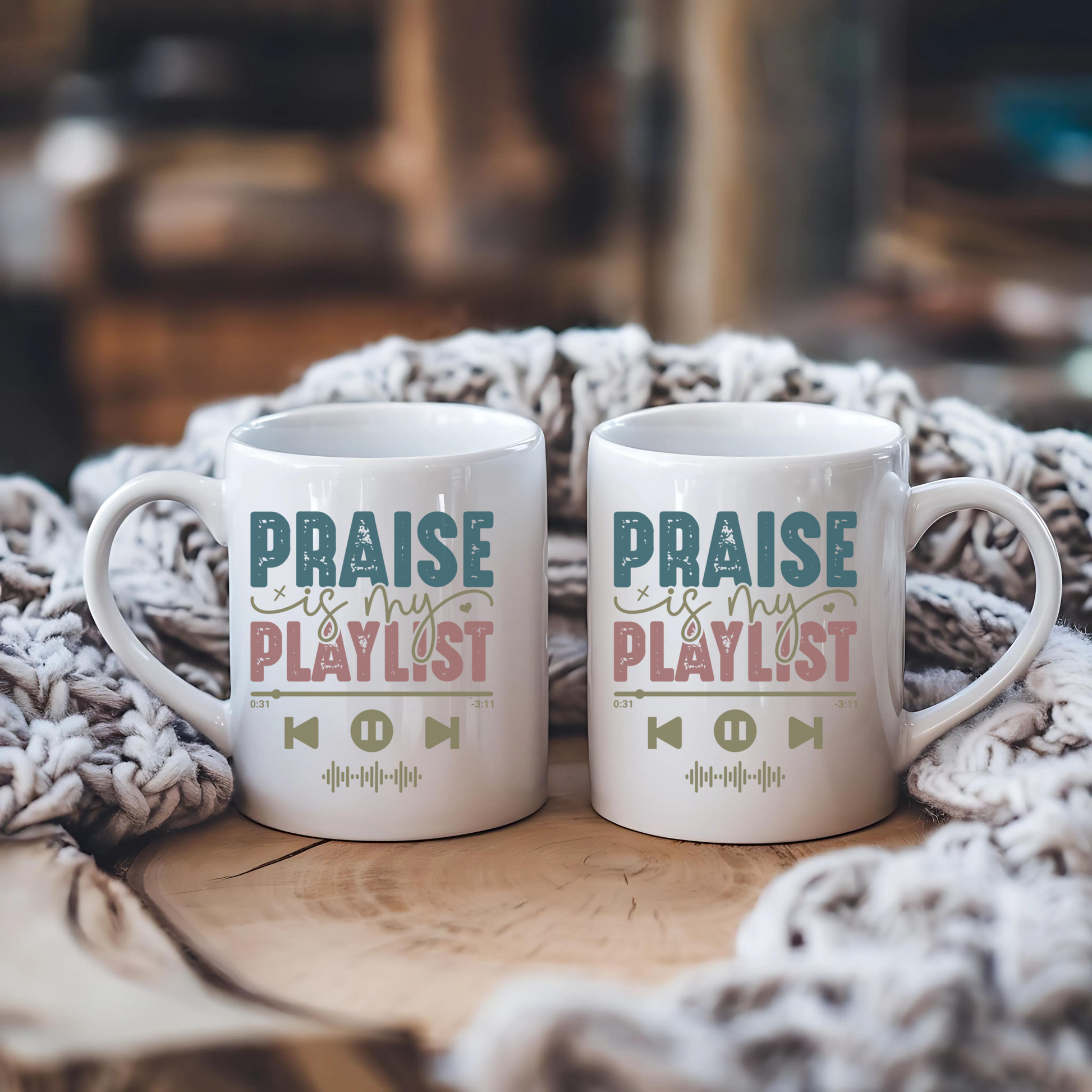 Two white mugs with 'Praise is my playlist' text on a wooden surface with a textured blanket.