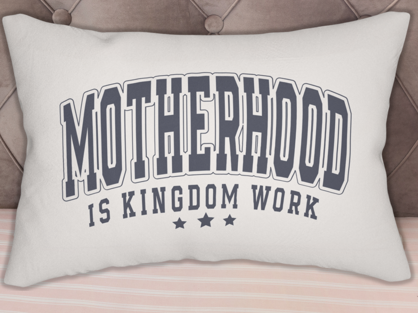 “Motherhood is Kingdom Work” pillow displayed against a tufted headboard with striped bedding.