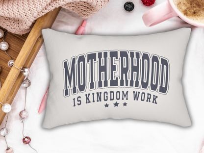 White lumbar pillow with bold navy text “Motherhood is Kingdom Work” styled with knit blanket, pearls, berries, and pink coffee cup.