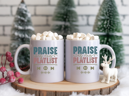 Two mugs with 'Praise is my playlist' text on a wooden stand with Christmas decorations.