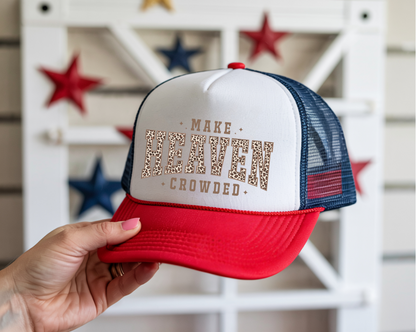 Trucker hat with 'Make Heaven Crowded' text held by a hand, with decorative stars in the background.