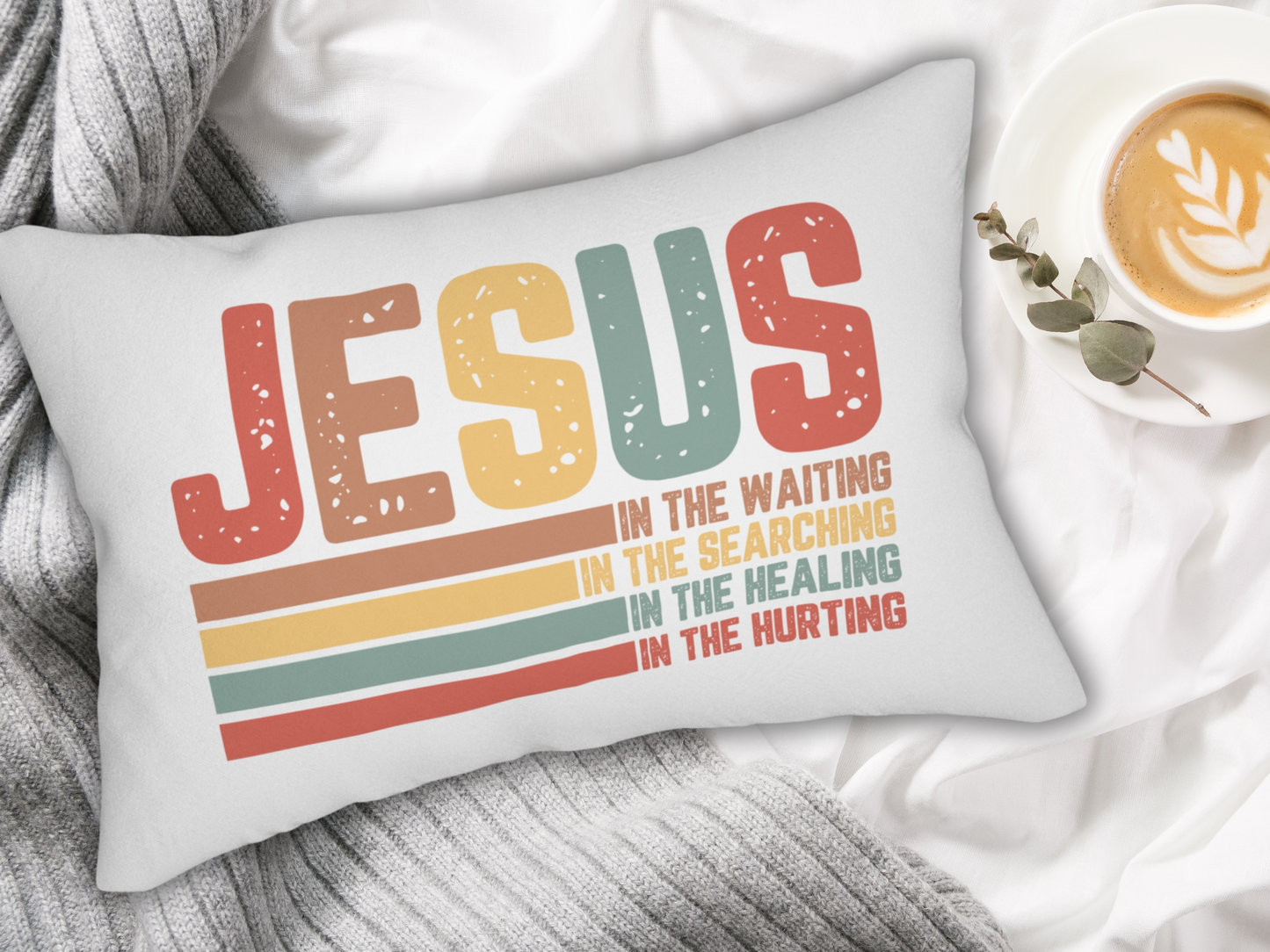 Pillow with gray knitted blanket, cup of latte, and eucalyptus on a white bed.