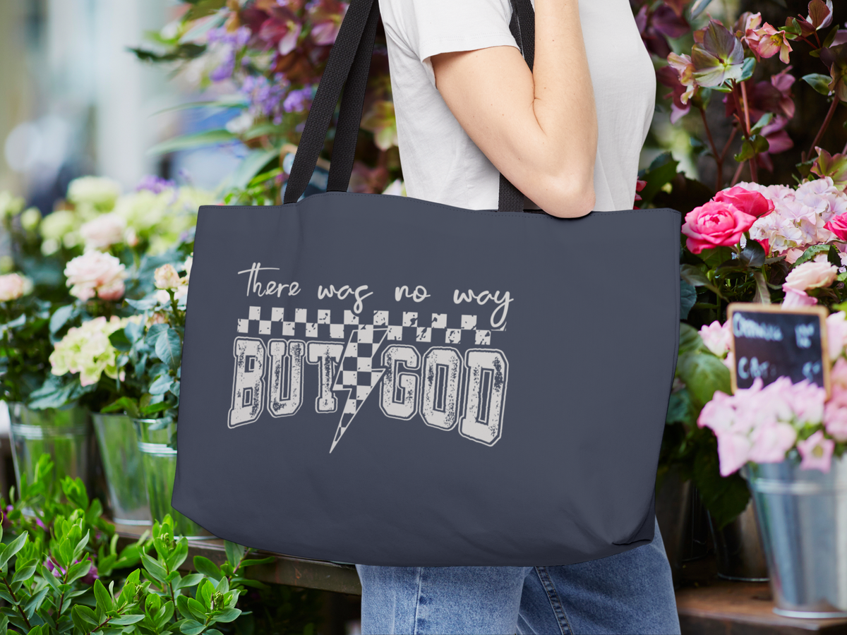 Woman carrying navy blue tote bag with “There was no way BUT GOD” design, standing near colorful flower shop display with roses and green plants.