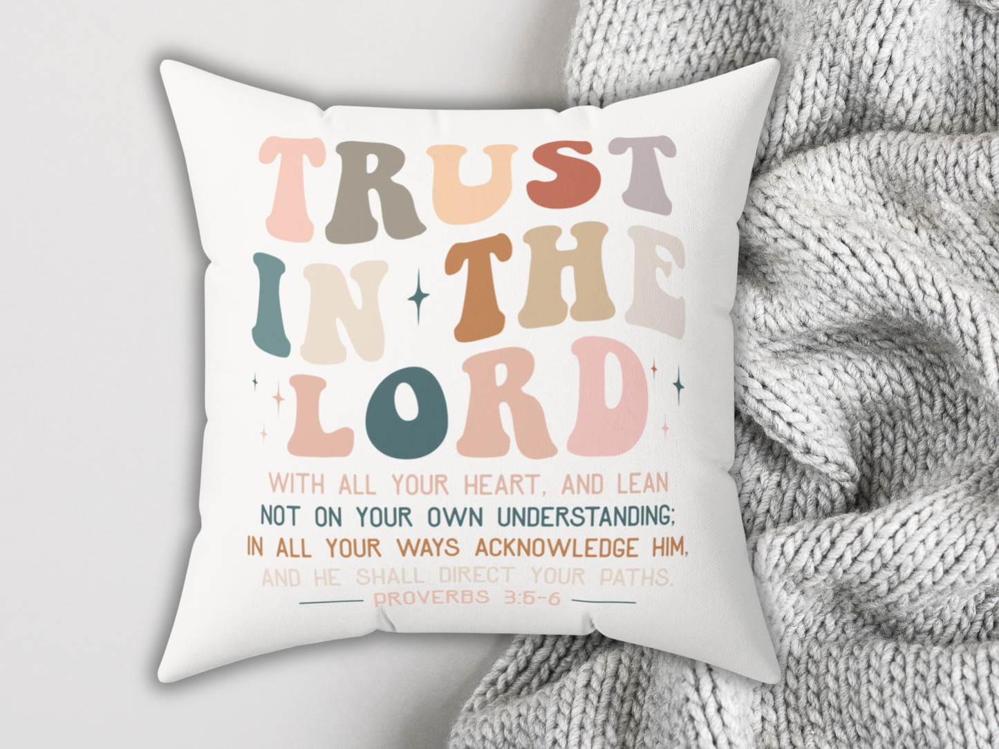 Inspirational Christian throw pillow with “Trust in the Lord” lettering, laid on soft gray knit blanket for cozy home decor.