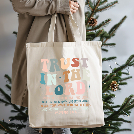 Tote bag with 'Trust in the Lord' text held by a person in front of a Christmas tree.