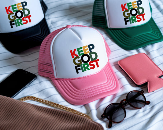 Pink cap with 'Keep God First' text on a white surface with sunglasses and phone.