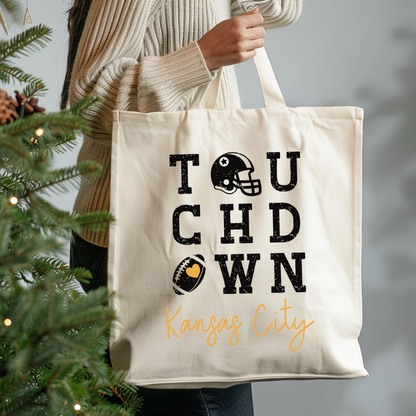 Tote bag with 'Touchdown Kansas City' text held by a person next to a Christmas tree.