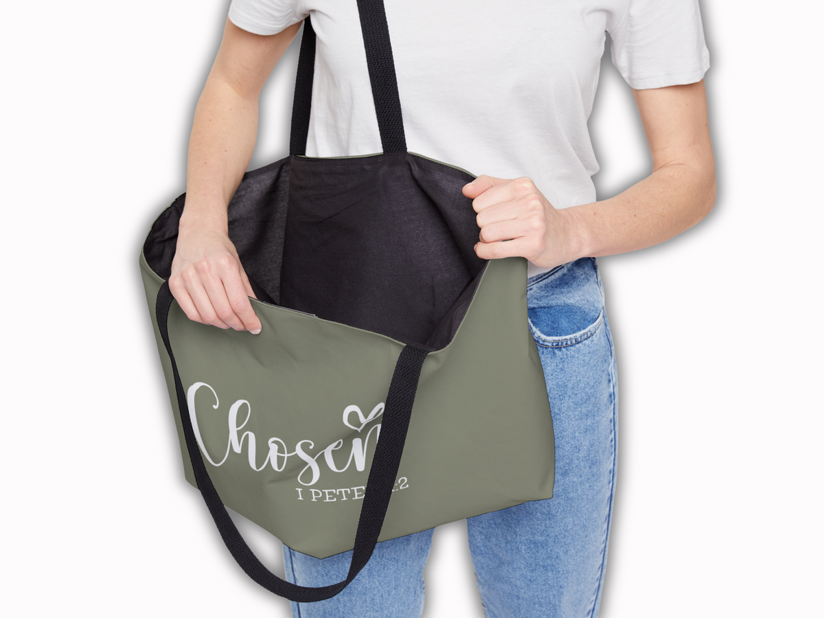 Person holding open the “Chosen” tote bag, showing spacious black-lined interior and durable black straps.