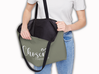 Person holding open the “Chosen” tote bag, showing spacious black-lined interior and durable black straps.